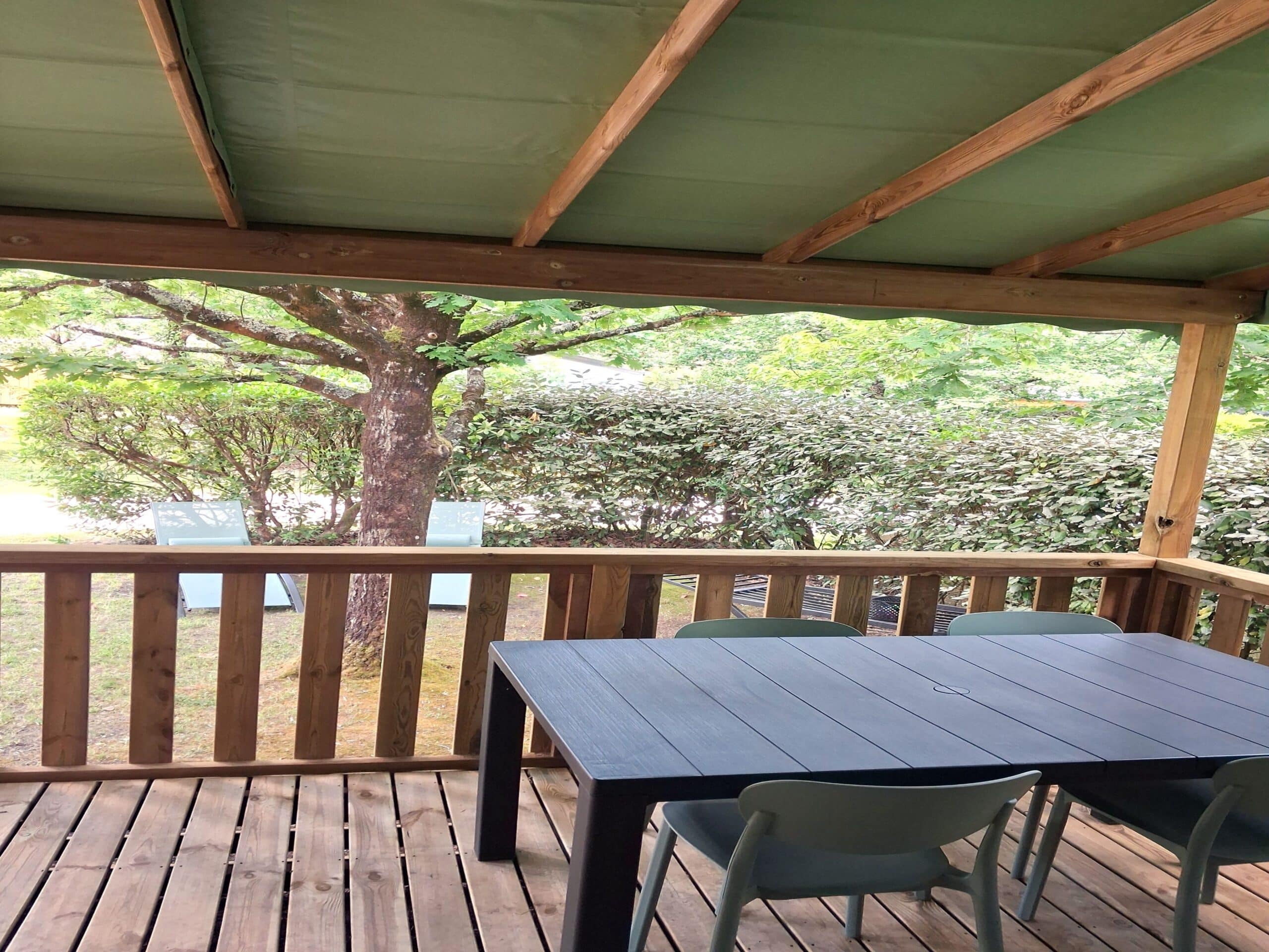 Terrasse en bois couverte avec table de jardin et chaises offrant une vue sur un extérieur verdoyant.