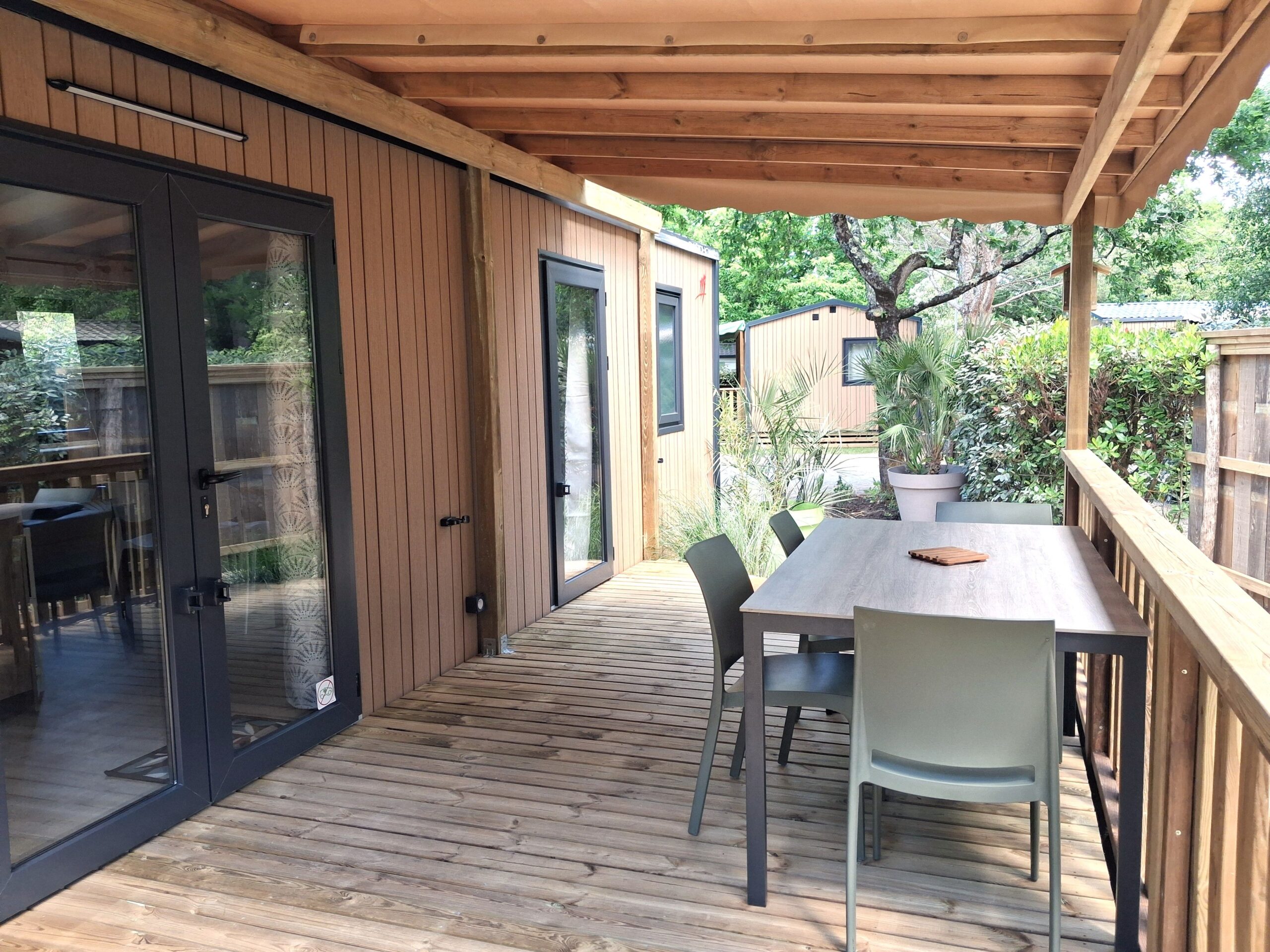 Terrasse en bois d'un mobil-home moderne avec table de jardin grise sous une pergola protectrice.