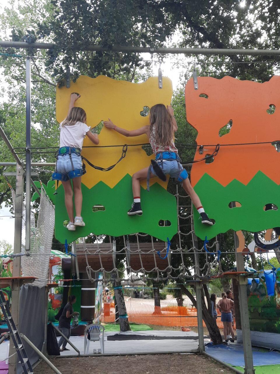 Deux filles escaladent un mur coloré dans un parc d'accrobranche, équipées de baudriers de sécurité.