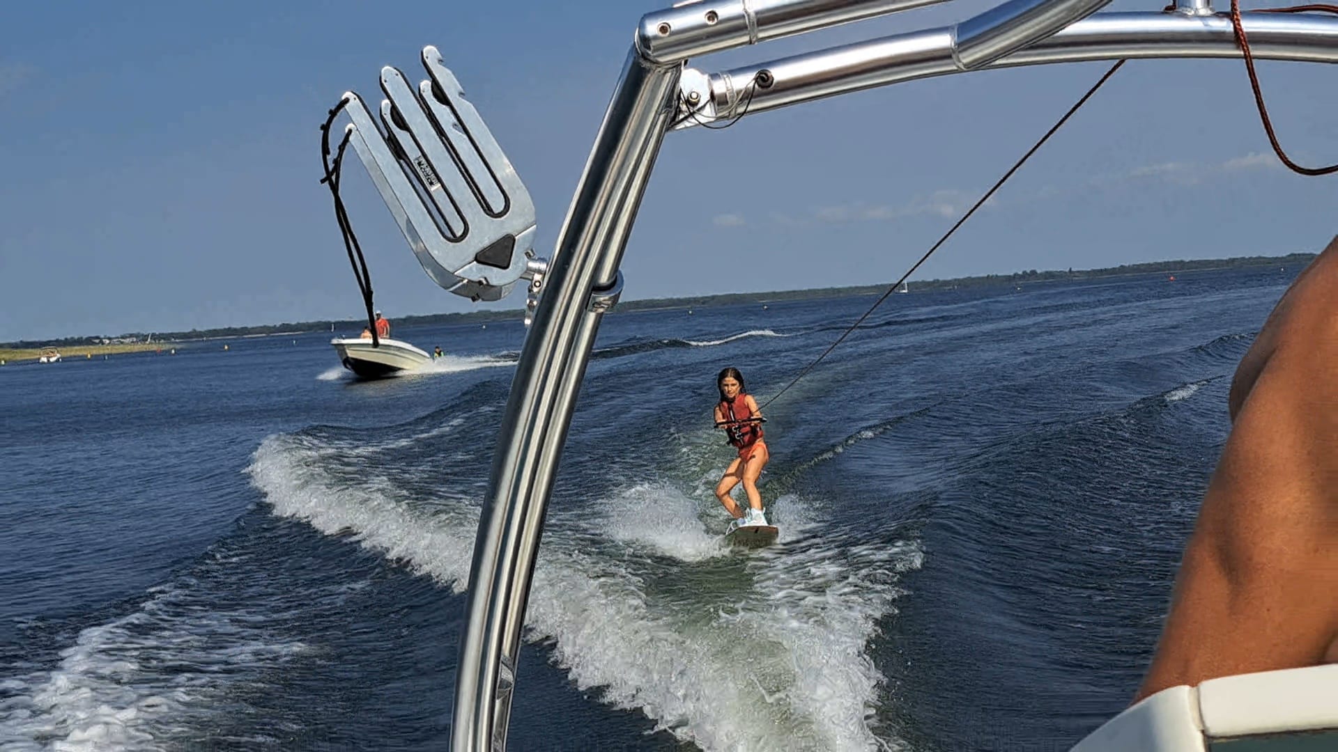 Jeune fille faisant du wakeboard sur le sillage d'un bateau, vue depuis une tour de wakeboard métallique.
