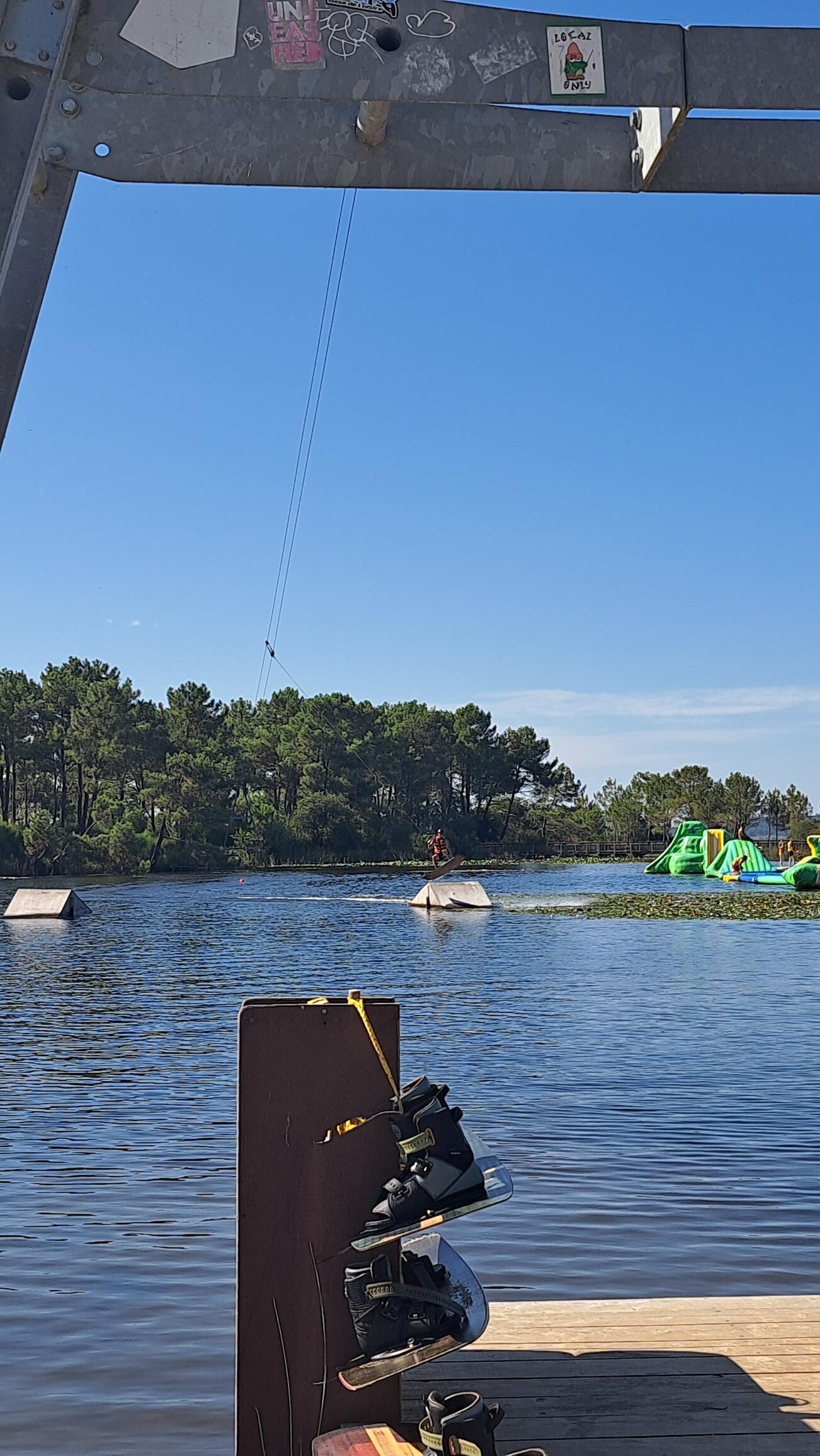 Wakeboarder sautant d'un tremplin dans un parc nautique par temps clair avec structures gonflables et forêt.